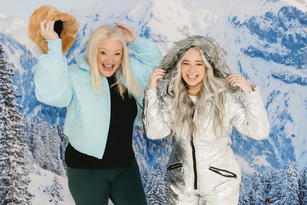 Friends in puffer jackets at an apres-ski photo booth with a snowy mountain backdrop. A photo booth setup we bring to Reno events