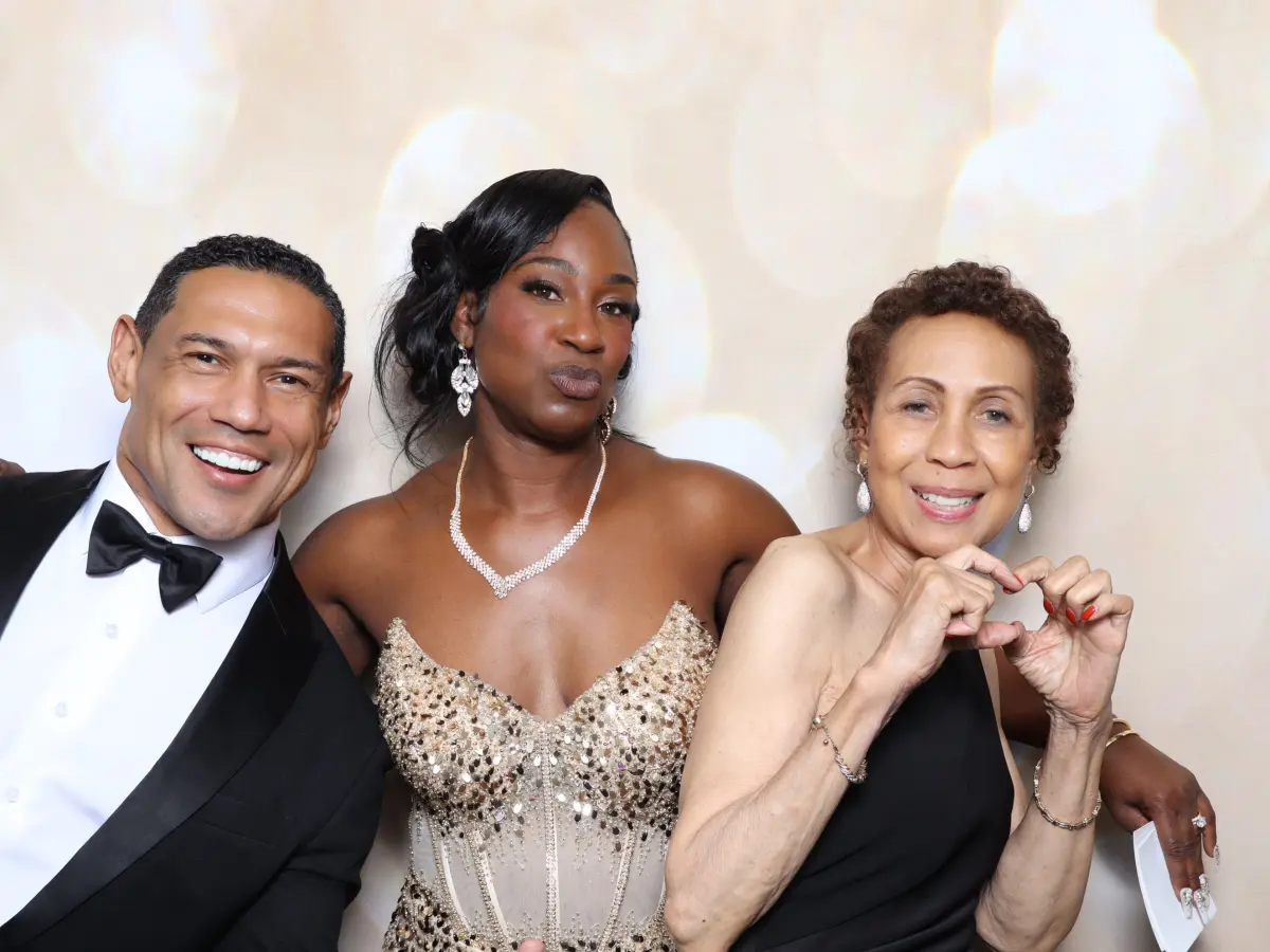 Three guests, one in a tuxedo and bow tie and one making a heart with her hands, posing at a gala photo booth