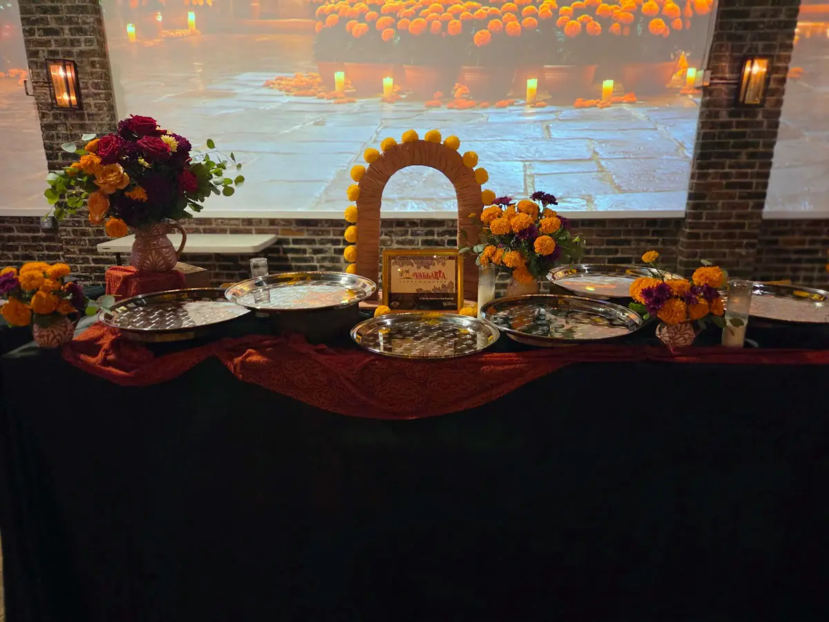 Marigold arch and silver trays on a Day of the Dead table at Candela La Brea, with projection-mapped walls behind