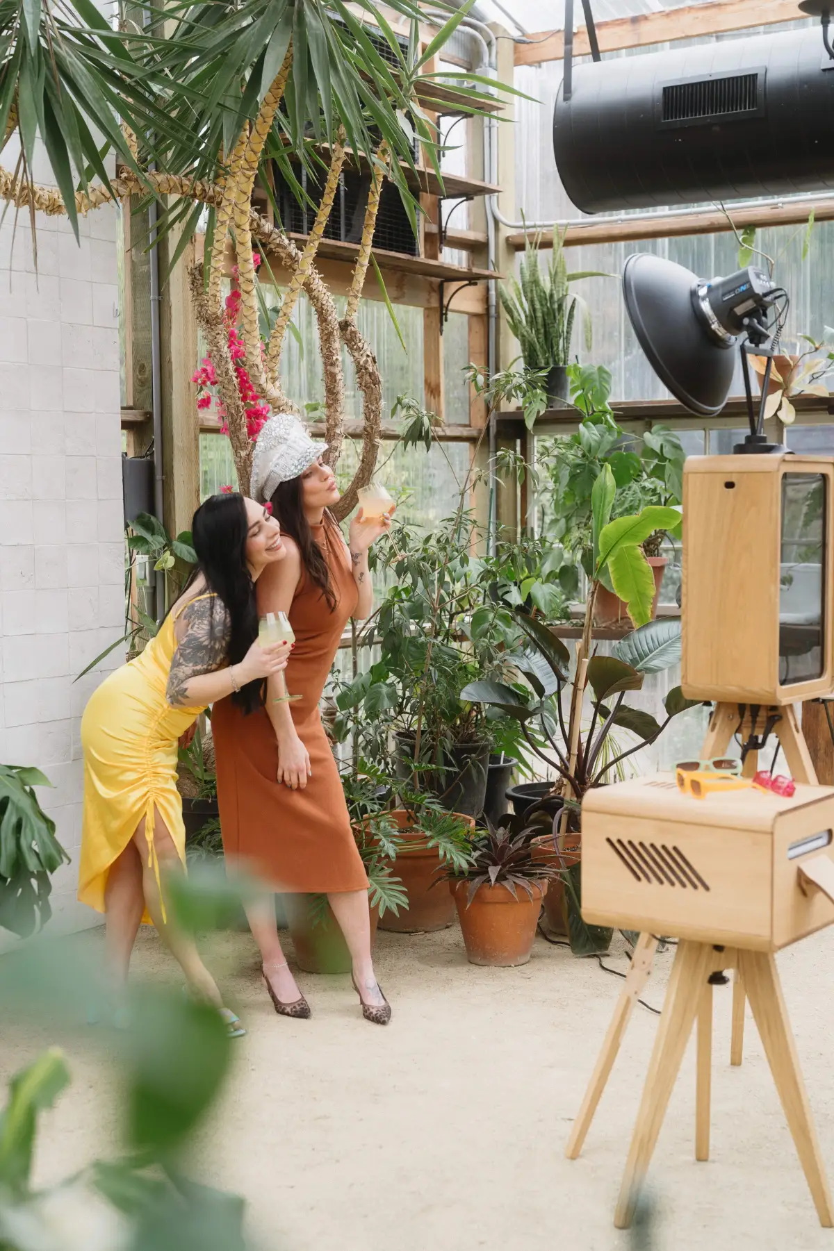 Two guests posing at The Oak Booth wood photo booth inside a plant-filled greenhouse venue in Los Angeles, Captured Celebrations