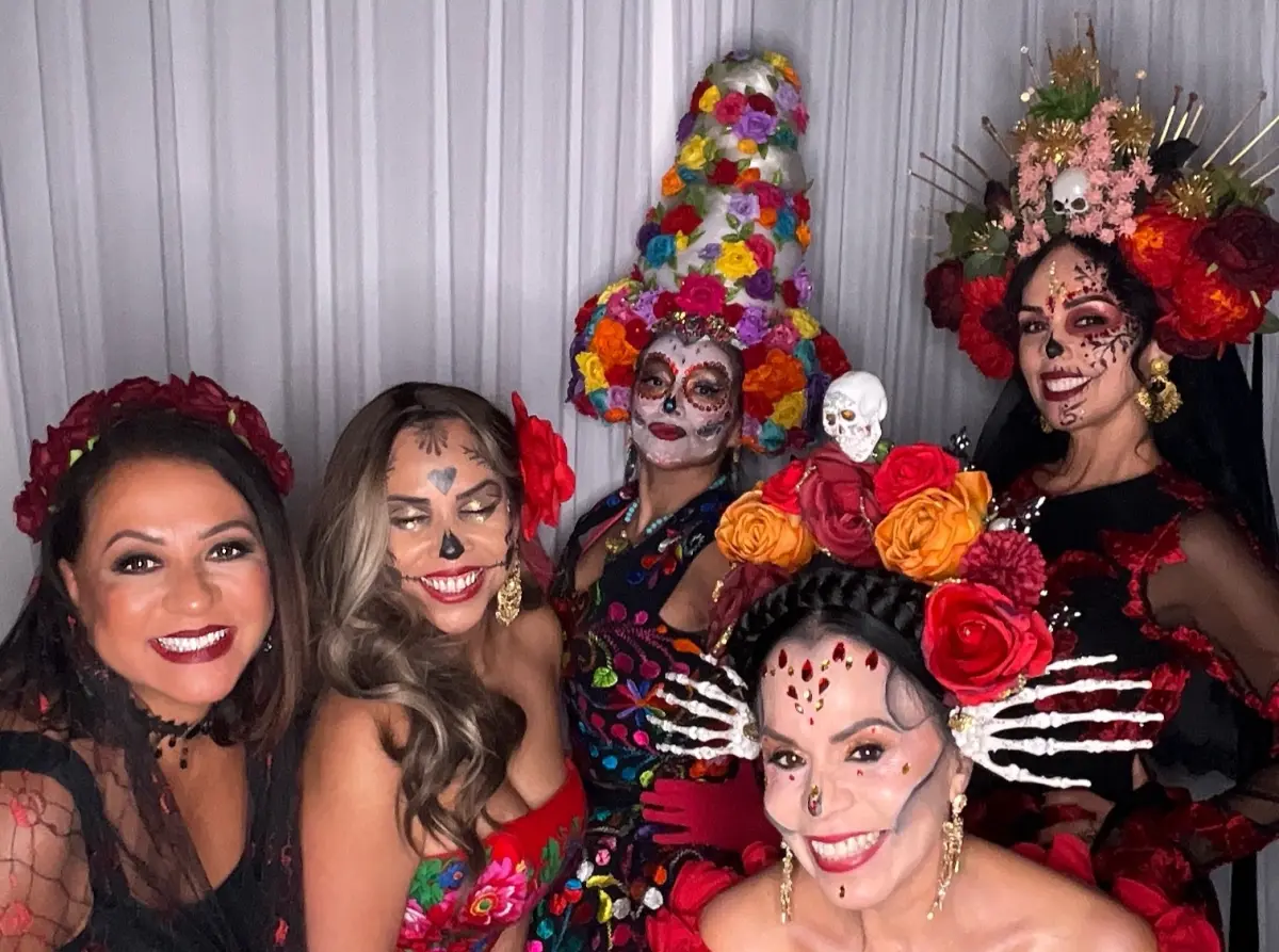Five guests in Catrina face paint and flower crowns smile at the white Glam photo booth at Candela La Brea in Los Angeles