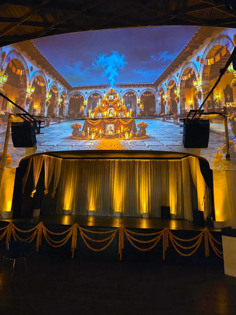 Stage at Candela La Brea in Los Angeles with a Day of the Dead courtyard projected across the walls and marigold garlands on the curtains