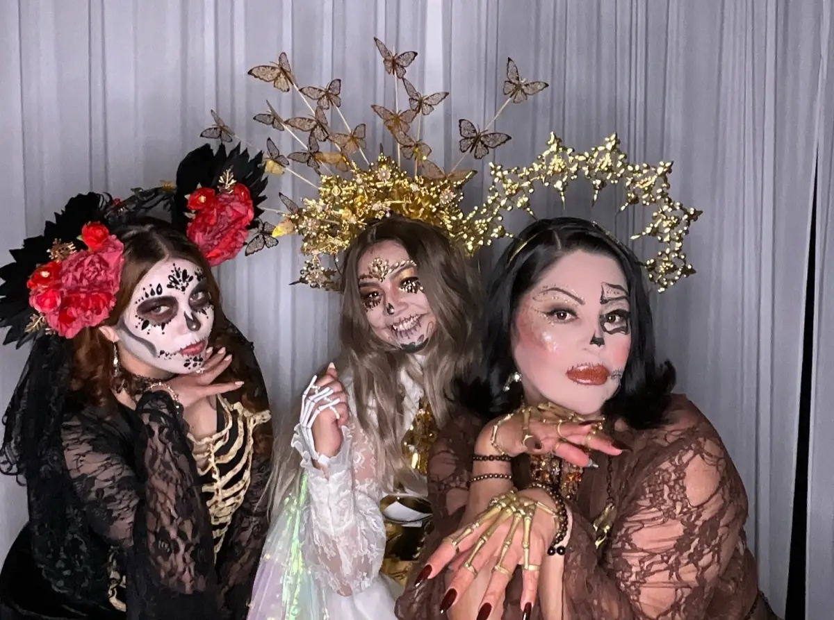 Three guests in black lace, skeleton makeup and gold halo crowns strike playful poses at a Catrina Ball in Los Angeles