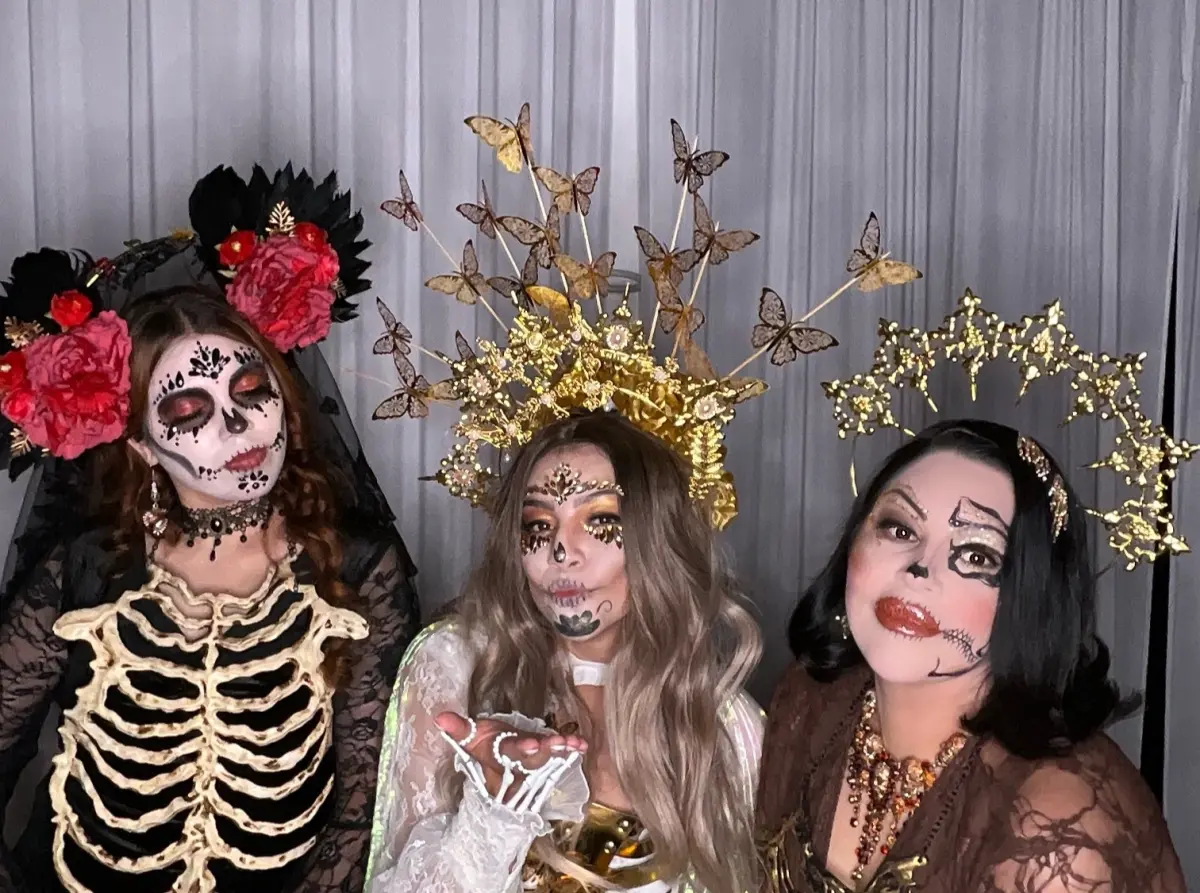 Three guests in skull makeup and gold butterfly crowns, one blowing a kiss, at the Los Angeles Catrina Ball