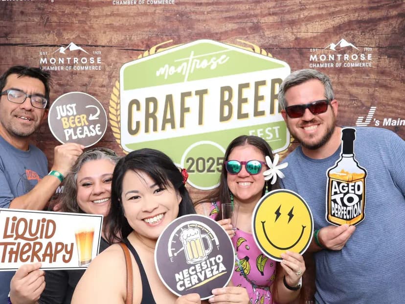 Group posing with beer-themed signs at Montrose Craft Beer Fest 2026 step-and-repeat