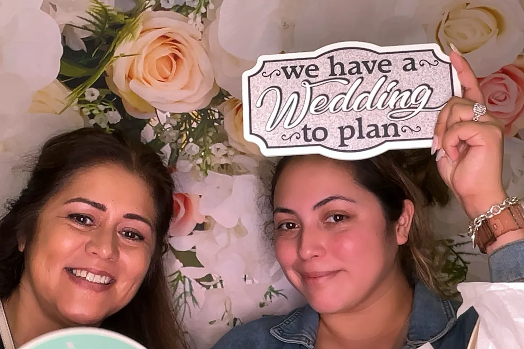 Two women smiling, holding "We have a Wedding to plan" sign