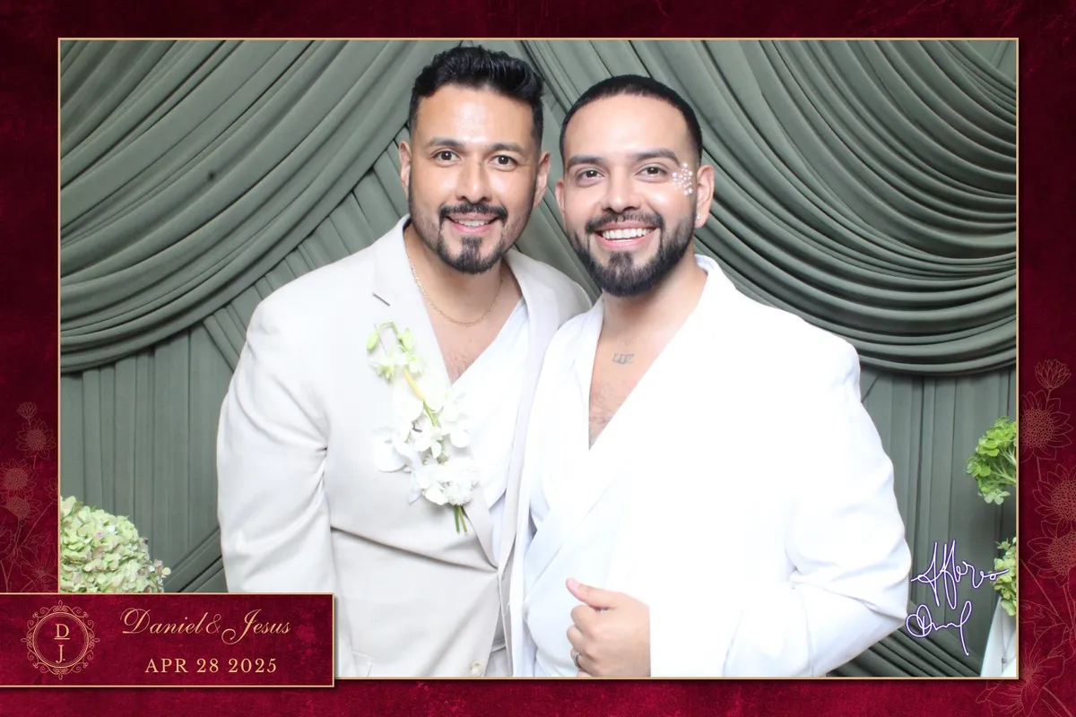 Two smiling men in light suits stand in front of green drapes. One wears a boutonnière. Red border reads "Daniel & Jesus APR 28 2025."