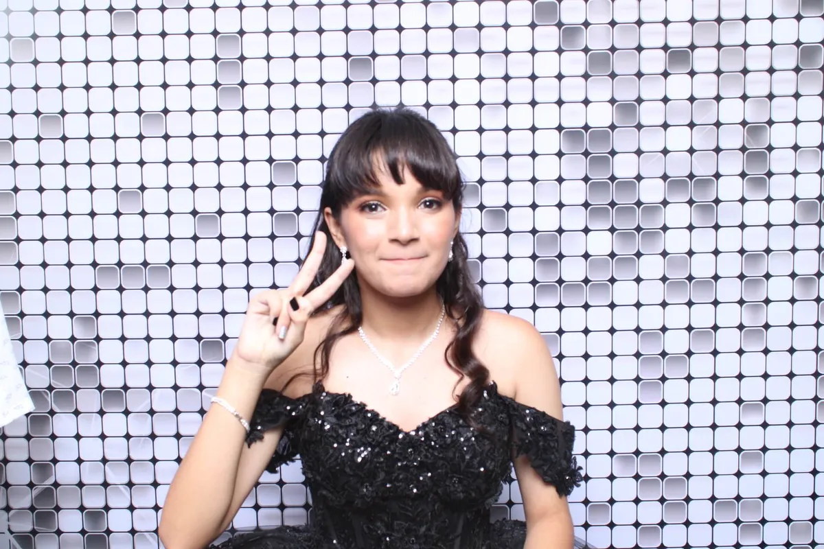 Quince in a black sequined dress flashes a peace sign. Background of white and gray tiles. Elegant, cheerful mood.