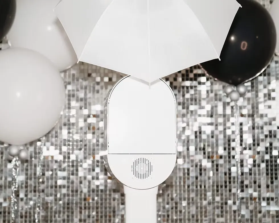 White photo booth with umbrella, surrounded by black and white balloons with a silver sequin backdrop, creating a festive atmosphere.