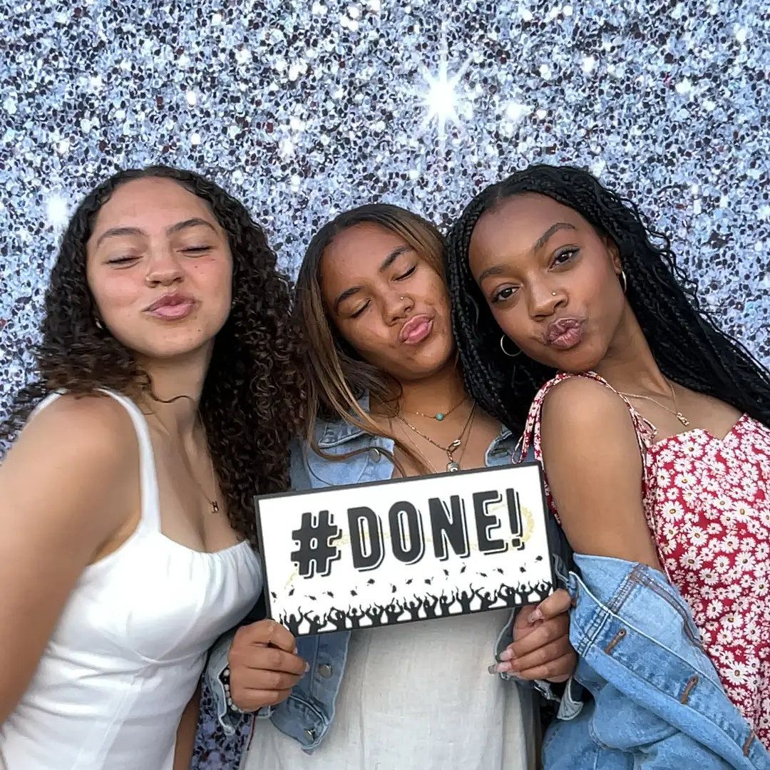 Three friends pose with '#DONE!' sign, graduation celebration